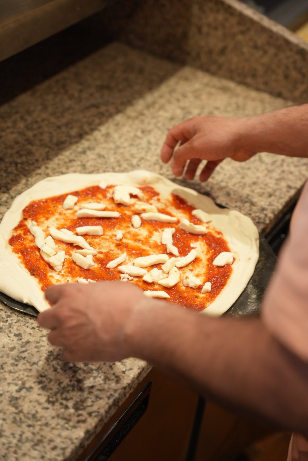 Pizza en préparation : pâte étalée à la main, sauce tomate et mozzarella ajoutées par le pizzaiolo