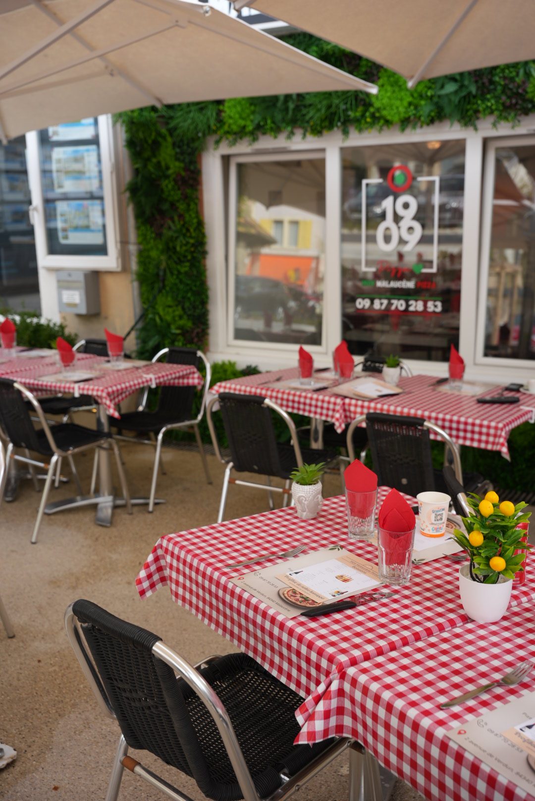 Tables en terrasse 1909 avec nappes vichy rouge et blanc, devant la vitrine au logo italien